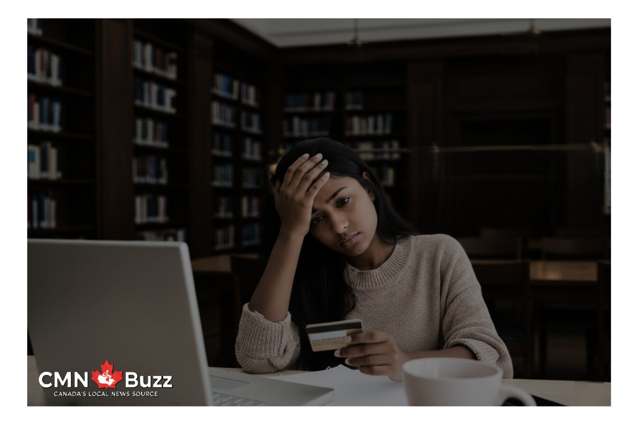 A stressed Indian female student sitting alone in a dark library in Canada, looking at her laptop and credit card, representing the 2026 student housing and financial crisis.